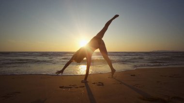 Gün batımında deniz kıyısında jimnastik yapan sağlıklı bir kadın.