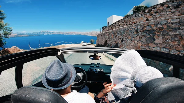 A young woman is driving by car to the sea and waving her hand from a convertible car. Vacation on the sea coast of Santorini island, greece