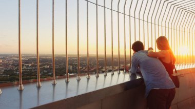 Münih, Almanya - 15 Ağustos 2018: Olimpiyat Kulesi 'nden gün batımında Münih' in havadan manzarasının keyfini çıkaran romantik genç çift