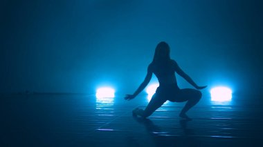 Zarif modern bale kadını stüdyoda mavi ışıklarla dans ediyor.