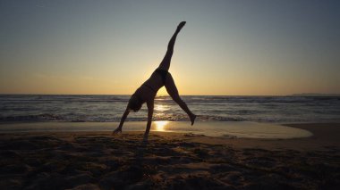 Gün batımında deniz kıyısında jimnastik yapan sağlıklı bir kadın.