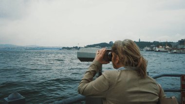 Sarışın kadın dürbün kullanarak gemileri, deniz manzarasını ve İstanbul 'un Asyalı tarafını izliyor. Uzaklara bakıyorum. Turistler için gözlem güvertesi