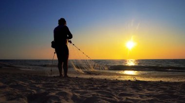 Kıyı balıkçıları okyanus kıyısında gün batımında ağlarını çekiyorlar.