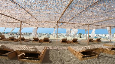 Lüks tatil beldesi kumlu bir plajda, mavi güneşli gökyüzünün arka planında beyaz çadır.