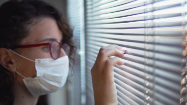 Virüs bulaşmış Corona virüsü kovid-19 kadın hastane odasında izole edilmiş ve koruyucu maske takan pencere perdelerine bakıyor.