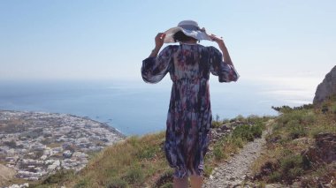Santorini 'deki Antik Thera dağında yürüyen bir kadın Kamari köyünün panoramik manzarasının keyfini çıkarıyor.