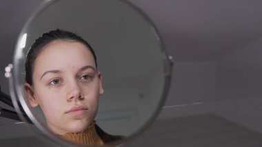Yüzüne fondöten ya da allık süren bir kadın daire aynasına bakıyor.