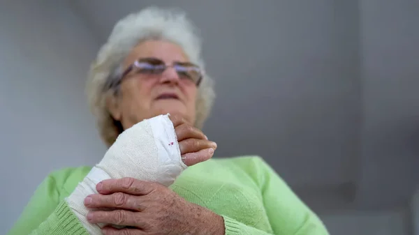 Old woman massage her injured broken hand sitting, cinematic dof