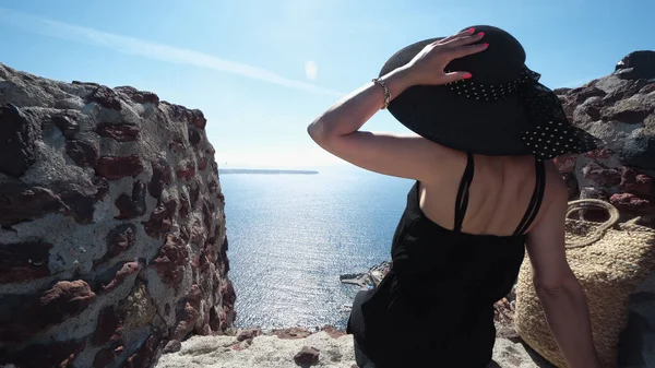 Czarna Elegancka Kobieta Santorini Siedząc Krawędzi Muru Zamku Patrząc Nadchodzący — Zdjęcie stockowe
