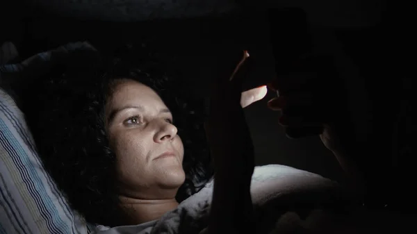 Lying relaxed woman watching online content on smartphone in the dark