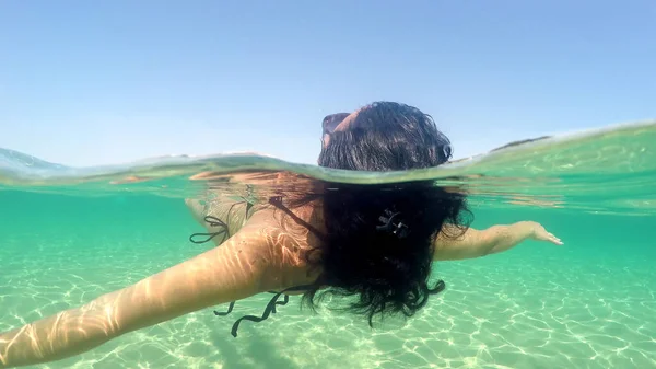 一个带着眼镜和比基尼的性感女人躺在海面上悠闲自在地躺着 从漂浮在波浪上挥动的相机看到了半边水下的凹凸圆顶镜头 — 图库照片