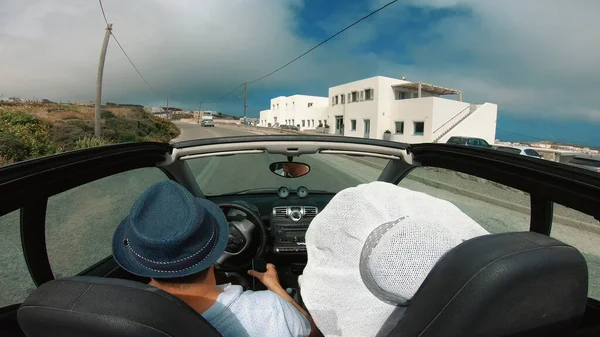 A young woman is driving by car to the sea and waving her hand from a convertible car. Vacation on the sea coast of Santorini island, greece