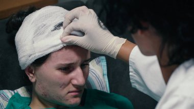 Doktor kafasında travma ve elastik bandajla bir hastanın kafasına dokunuyor. 