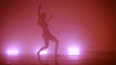 Dans eden, karanlık dumanlı stüdyoda eğitim gören genç bir kadının silueti. Sokak hip hop dansçısı. Spor salonunda egzersiz.
