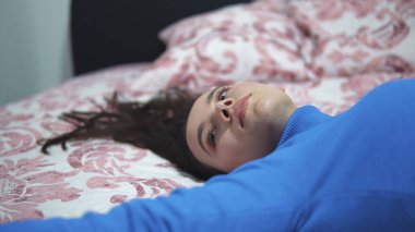 Genç düşünceli bir kadın sabah geç saatte yatakta uzanıyor. Yatakta gözleri kapalı, dirseklerini uzatarak uykulu bir gülümseme sergiliyor.