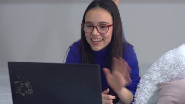 Bilgisayarı kullanan gülümseyen genç bir kadın. İnternette eğleniyor ya da yatakta uzanırken arkadaşlarıyla sohbet ediyor.