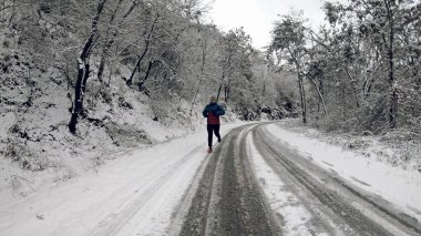 Genç sağlıklı sporcu karlı dağ yolunda asfalt yolda koşuyor.