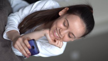 Ergenlik öncesi ergenlik çağındaki bir kız evde yatakta yatarken akıllı bir telefonla kaydırma yapıyor, dikey yönelim.