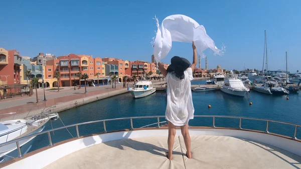 Fashion model woman in white dress standing on luxury yacht boat deck. Panoramic view of pier in Hurghada, Egypt