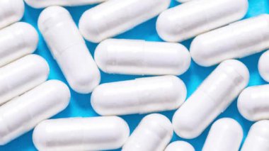 Bir sürü beyaz hap, kapsül, vitamin, pembe renkli arka planda uyuşturucu.