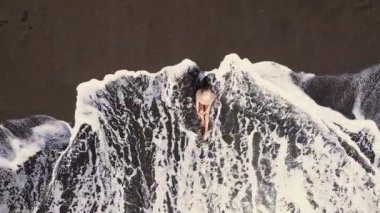 Kumlu sahilde oturan tanınmayan genç kadın kıyı şeridi dalgaları, hava manzarası....