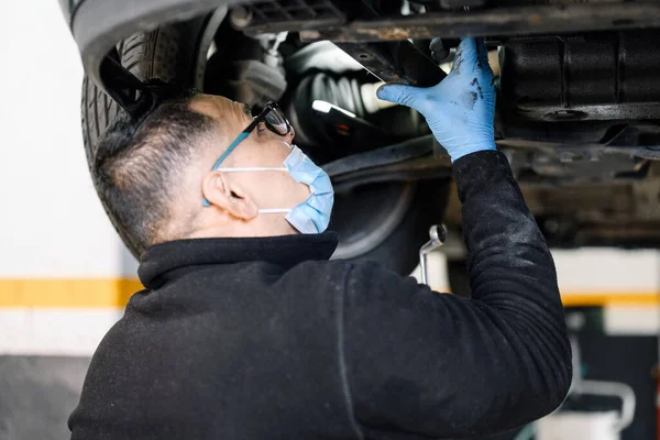 Auto mecánico hombre con mascarilla de trabajo en taller de reparación de automóviles. — Foto de Stock