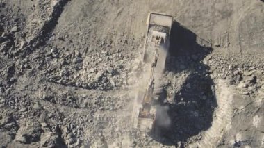 Toprağı hareket ettiren ve inşaat alanında çöp kamyonuna boşaltan kazıcının hava görüntüsü..