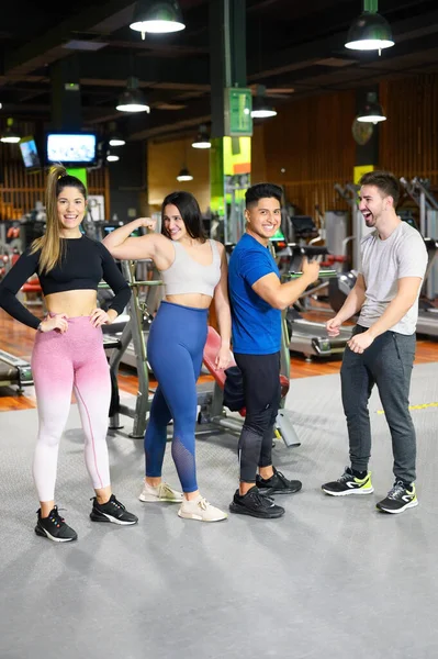 Groep van vier gelukkige vrouwelijke en mannelijke jonge volwassenen staan samen als goede vrienden, poseren in de sportschool. — Stockfoto