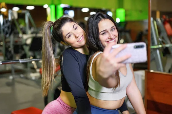 Portret van twee lachende sportieve vrouwen die een selfie foto maken in de sportschool. — Stockfoto