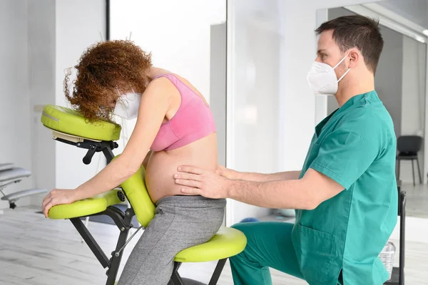 拍年轻理疗师按摩孕妇背。新常态下戴防护口罩的男子. — 图库照片
