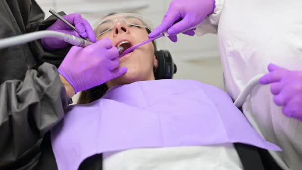 Молода жінка відвідує стоматологічну клініку для професійного лікування зубів. Доктор тримає інструмент . — стокове відео