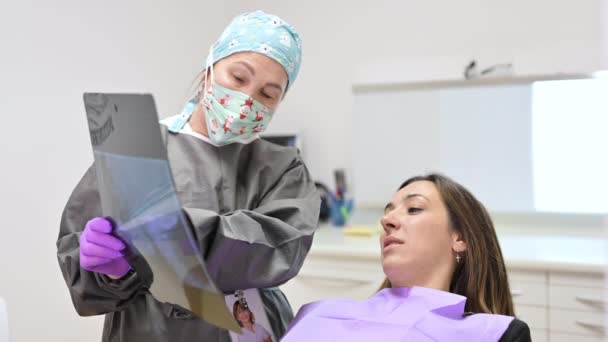 Doktor dişçi hastaların dişlerini röntgende gösteriyor. — Stok video