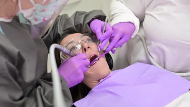 Jonge vrouwelijke patiënt bezoeken tandarts kantoor.Mooie vrouw zitten aan tandartsstoel met open mond tijdens orale controle terwijl arts werken aan tanden — Stockvideo