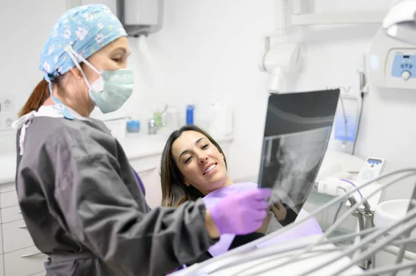 Dentista feminina apontando para pacientes radiografia em consultório odontológico. — Fotografia de Stock