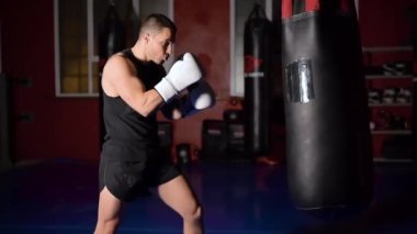 Kas yakışıklı kickboks dövüşçüsü antrenman turunda ağır çekimde boks çantasıyla sert bir tekme atıyor..