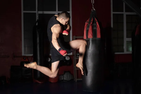 Kickboxing μαχητής Εκτέλεση Jumping Air Kicks με το γόνατο στην τσάντα Punch. Caucasian Man Εξάσκηση Πολεμικές Τέχνες Εκπαίδευση στο Αστικό Γυμναστήριο. — Φωτογραφία Αρχείου