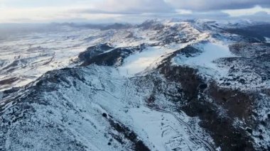 Bulutlu gökyüzünün altındaki kar dağlarının hava manzarası. Kış İHA görüntüleri