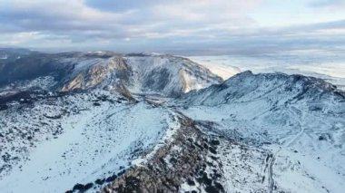 Bulutlu gökyüzünün altındaki kar dağlarının hava manzarası. Kış İHA görüntüleri