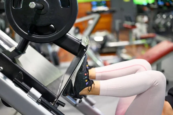 Zijaanzicht van fit jonge sportvrouw flexen haar benen spieren op de sportschool. Stockfoto