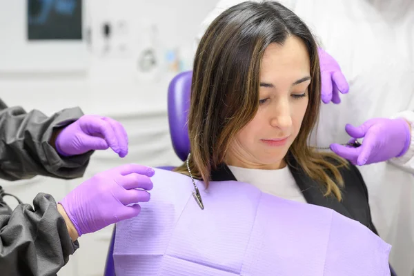 Medical secretary preparing dental treatment putting on dental bib on patient.