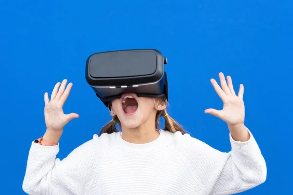 Jong meisje met een virtual reality bril. Geïsoleerd op blauwe achtergrond. VR-headset. Stockafbeelding