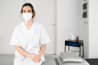 Modern klinikte, koronavirüs salgını sırasında koruyucu maske takan dost canlısı kadın fizyoterapist.