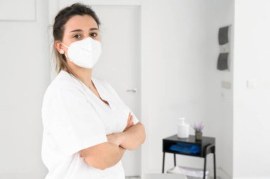 Koronavirüs salgını sırasında koruyucu maske takarak modern klinikte poz veren kendinden emin kadın fizyoterapist.