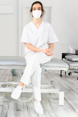 Modern klinikte, koronavirüs salgını sırasında koruyucu maske takan dost canlısı kadın fizyoterapist.