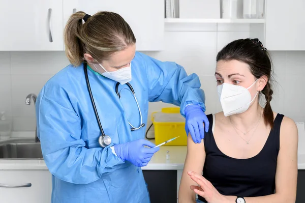 Jonge vrouw in het gezicht masker bang voor coronavirus vaccin, niet laat arts injectie in de kliniek. Vrouw bang voor covid-19 vaccinatie. Immunisatie tegen het wereldwijde virusconcept. Rechtenvrije Stockfoto's