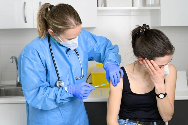 Jonge vrouw in het gezicht masker bang voor coronavirus vaccin, niet laat arts injectie in de kliniek. Vrouw bang voor covid-19 vaccinatie. Immunisatie tegen het wereldwijde virusconcept. Stockfoto