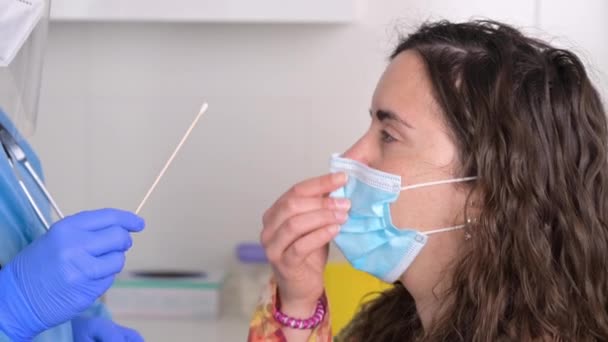 Медсестра в защитном костюме берет образец носового мазка у молодой пациентки. COVID-19. — стоковое видео