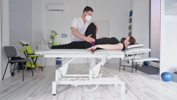 Brede hoek schot van fysiotherapeut stretching patiënt op massagetafel in het ziekenhuis. — Stockvideo