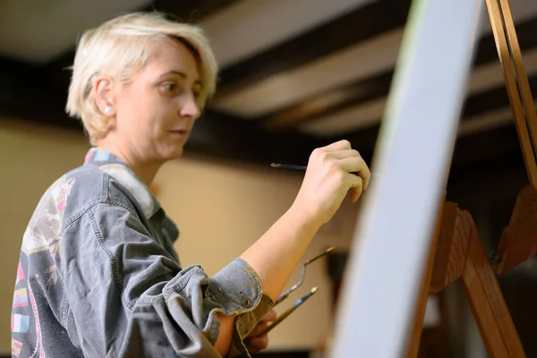 Kvinnlig kreativ konstnär konstnär koncentrerad och inspirerad målning bild med pensel och oljefärger på duk. — Stockfoto
