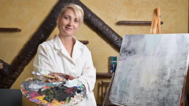 만족 스러운 여성 미술가가 이젤 옆의 새로운 그림 근처에 포즈를 취하는 모습 — 비디오